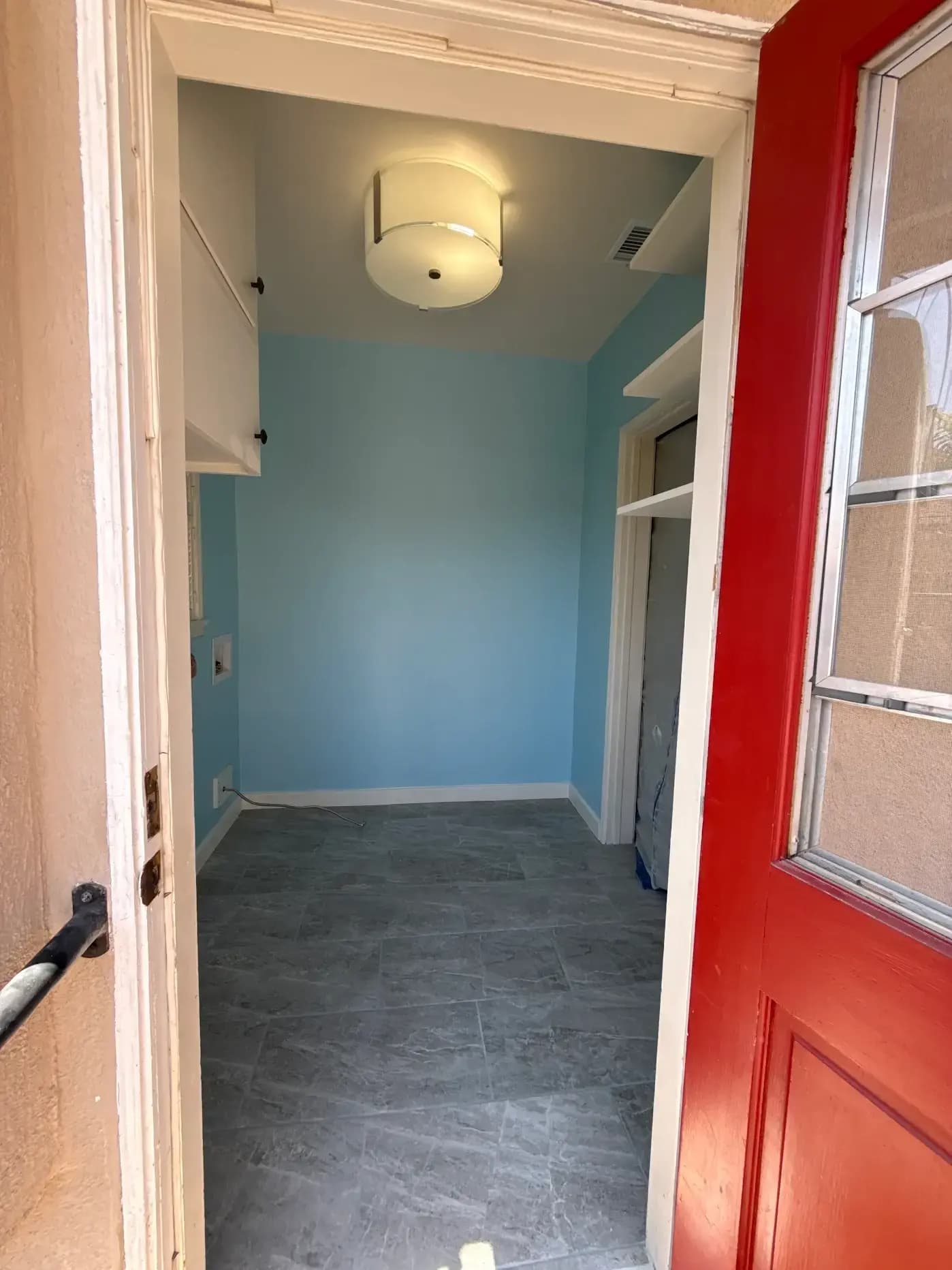Finished laundry room seen through doorway with red door, white cabinetry and utility hookups
