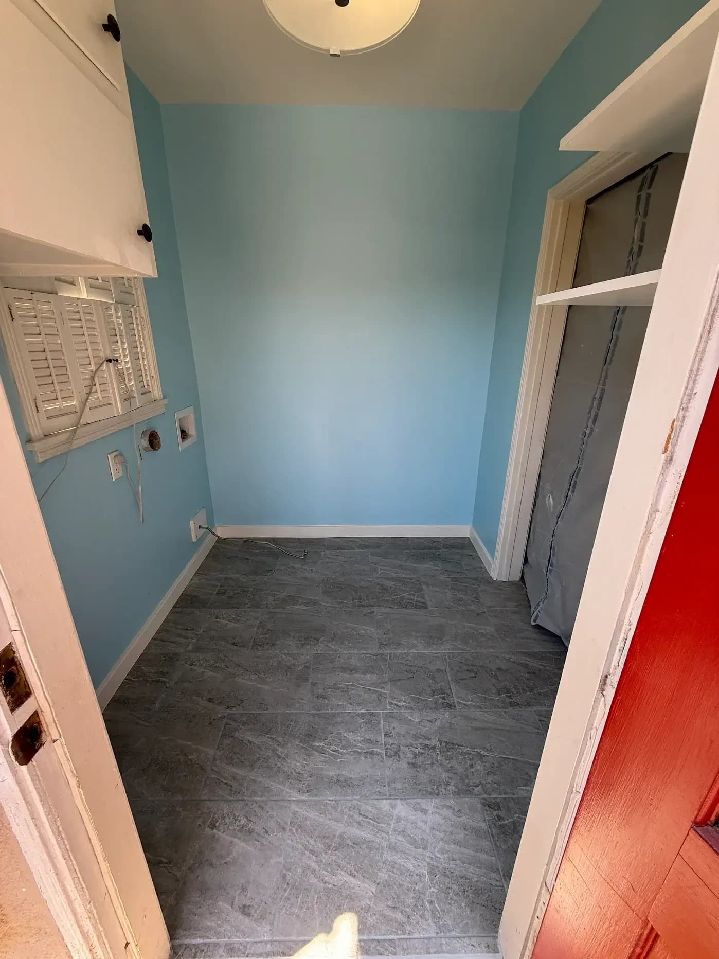 Wide interior view of finished laundry room with red door, blue walls, and grey tile flooring