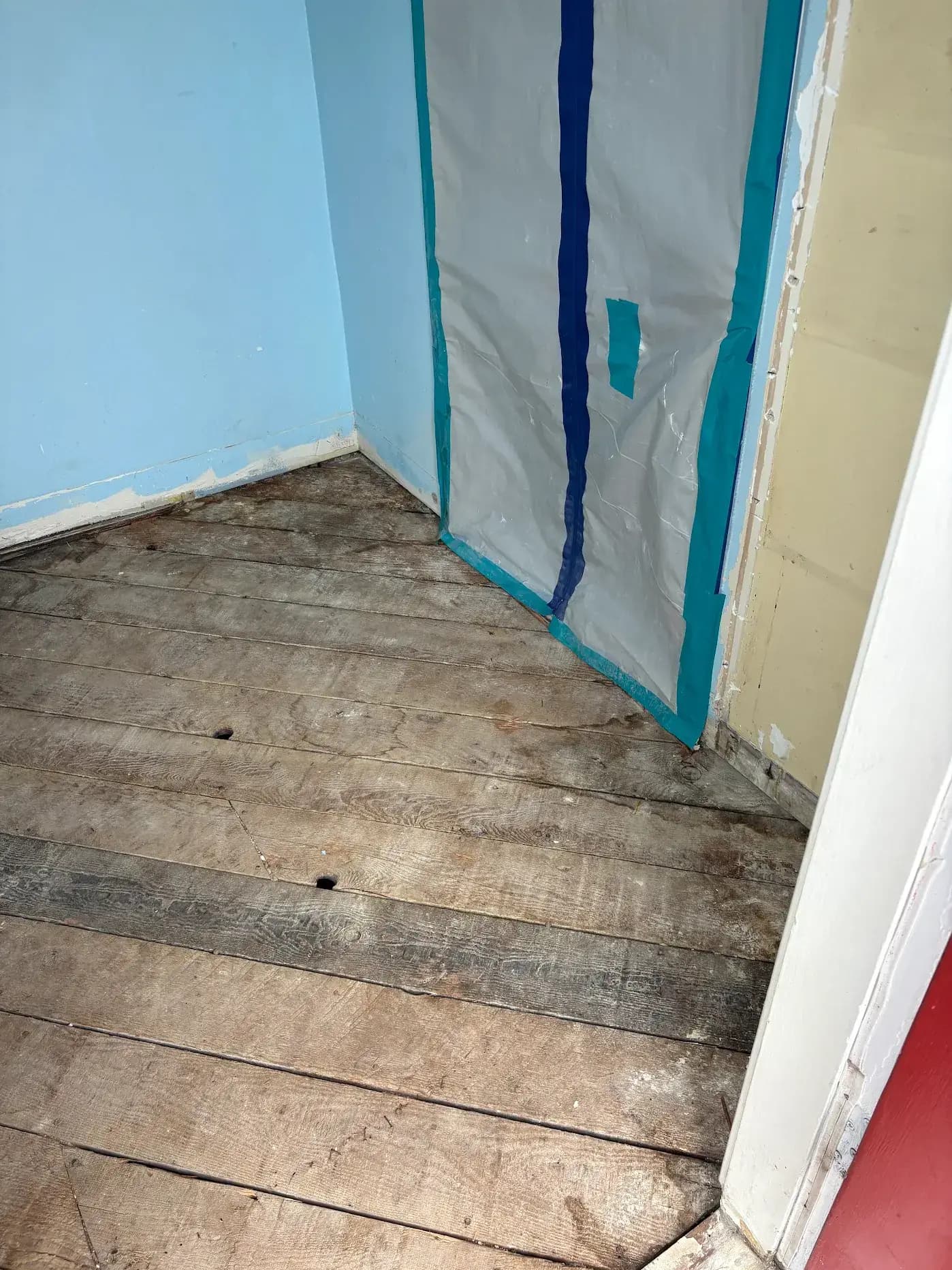 Laundry room before remodel showing old wood flooring, peeling paint, and water damage