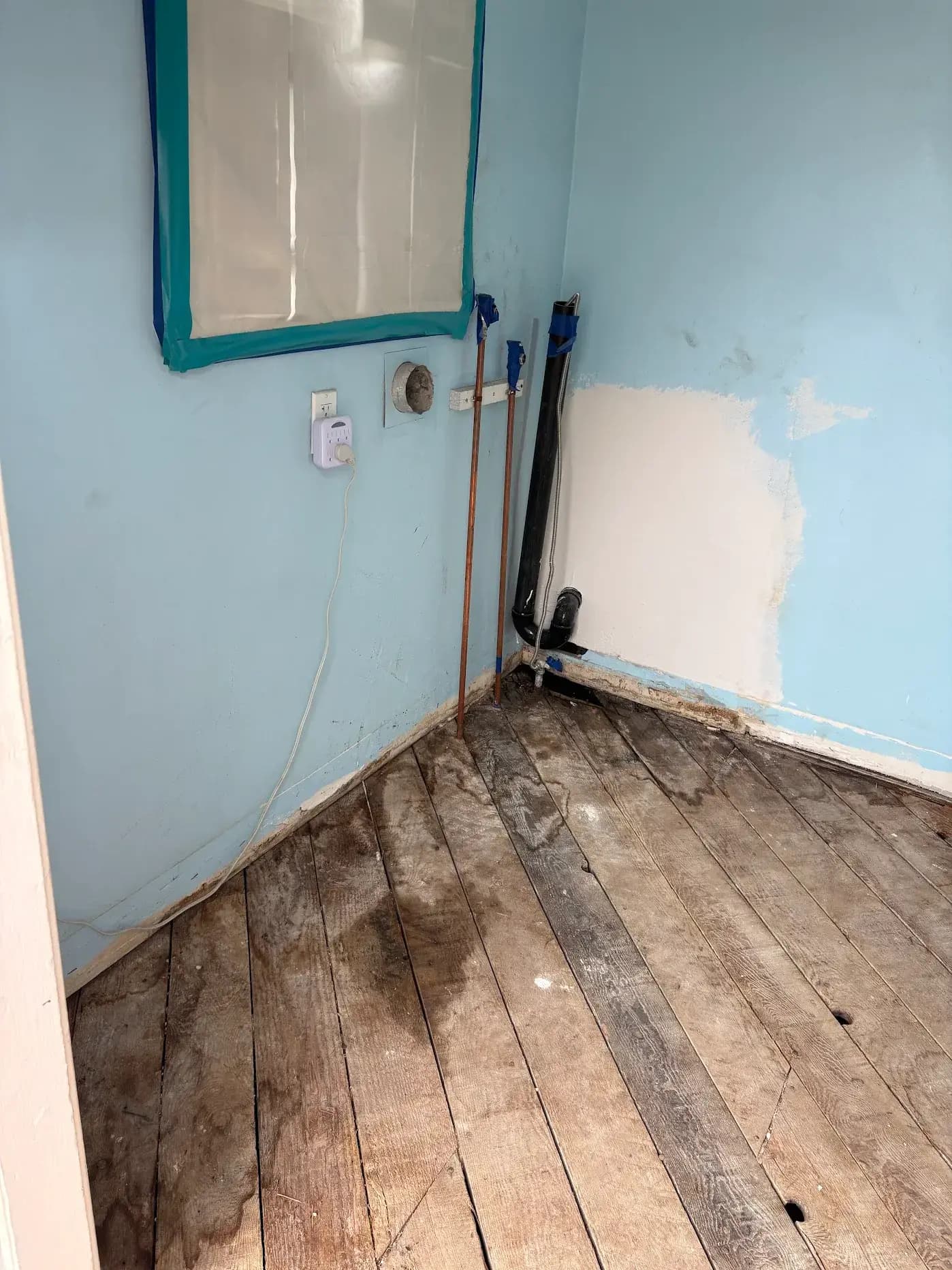 Laundry room mid-remodel with blue walls, drywall repair patch, and covered window
