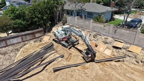 Excavator positioning steel I-beams on a sloped residential site