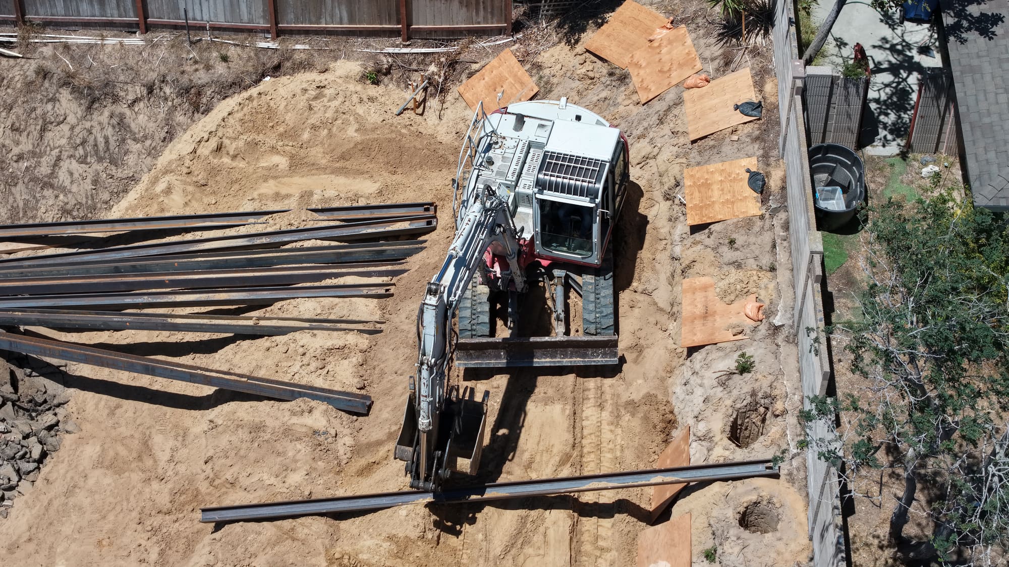 Top-down drone photo of caisson excavation, staged beams, and access protection